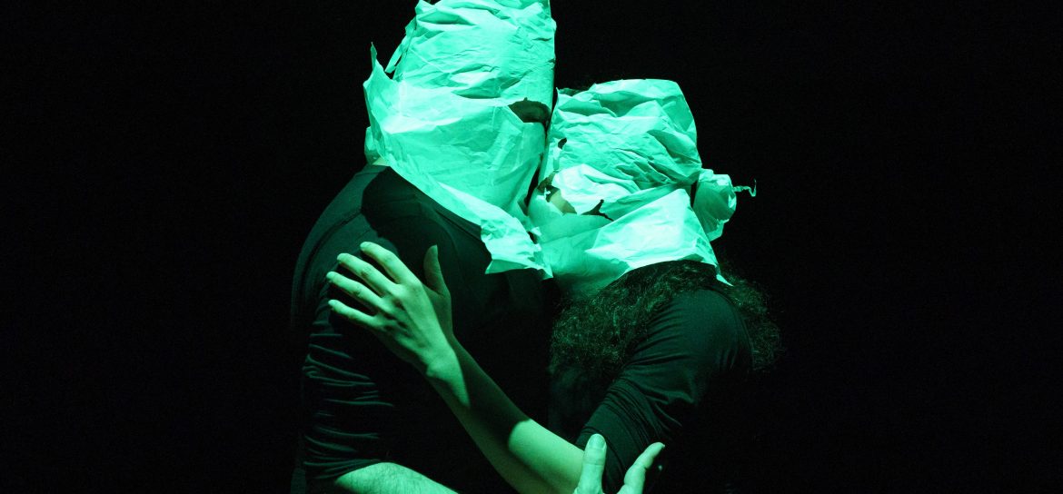 Dans un éclairage verdâtre et sur fond noir, Nasim et Kiasa se prennent dans les bras. Leurs têtes sont recouvertes de papier avec uniquement des trous pour les yeux.