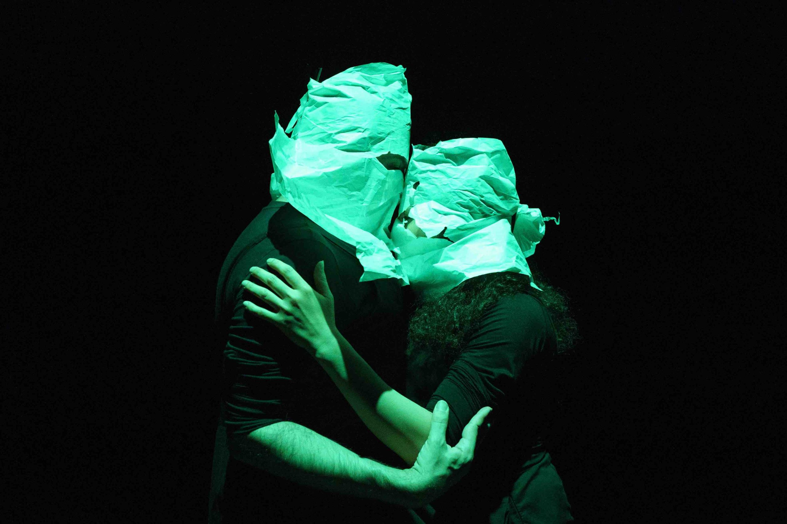 Photo de l'œuvre l'Inconsistance.
Dans un éclairage verdâtre et sur fond noir, Nasim et Kiasa se prennent dans les bras. Leurs têtes sont recouvertes de papier avec uniquement des trous pour les yeux.
