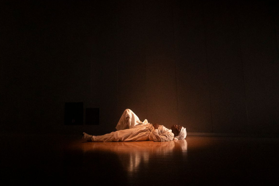 Spectacle Traceable de Nubian Néné : Nubian Néné est couchée au sol, habillée en blanc, dans la pénombre.
